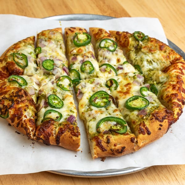 A sliced pesto pizza with melted cheese, red onions, and green jalapeño slices on a metal tray.